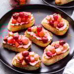 Six Goat Cheese Crostinis topped with Cranberry Apple Compote on a black serving plate with a jar of the compote behind them.