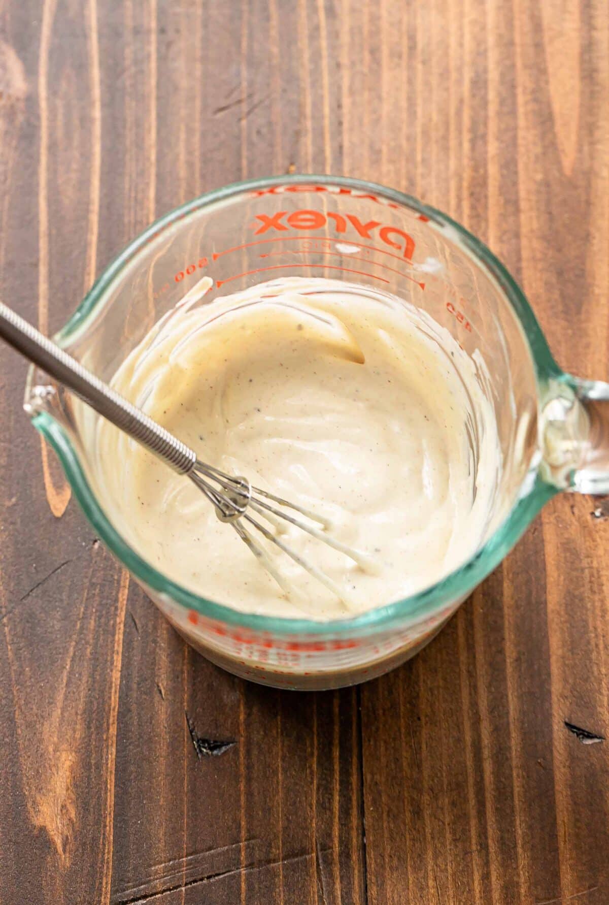 Dressing for chicken salad in a glass measuring cup with a whisk.