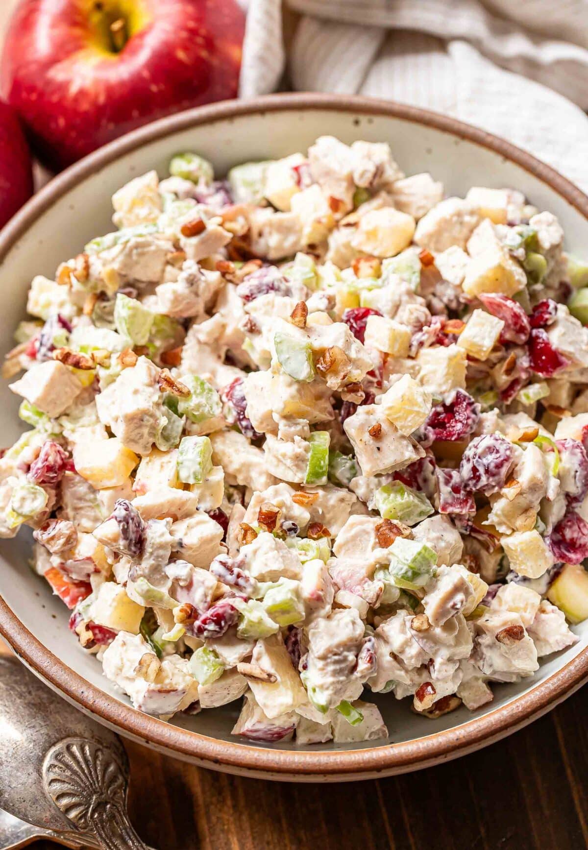 Chicken salad in a white serving bowl with an apple behind it.