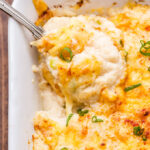 Serving spoon scooping out some of the Cheesy Cauliflower Casserole in a white casserole dish.