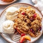 Cranberry Apple Pear Crisp on a white plate with with a for and two scoops of vanilla ice cream.
