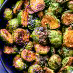 Closeup overhead photo of chili honey lime roasted brussels sprouts in a blue serving bowl.