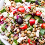 Mediterranean Lentil Salad in white bowl. Made with lentils, cucumbers, tomatoes, olives, feta and herbs.