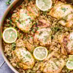 Skillet Greek Lemon Chicken and Rice in a metal sauté pan. Topped with slices of lemon and fresh herbs.