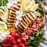 California Cobb Salad on platter with grilled chicken, strawberries, avocado slices, hard boiled eggs, bacon and goat cheese.
