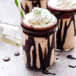 Irish Whiskey Coffee Milkshakes in mason jars drizzled with chocolate syrup and topped with whipped cream.