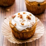 Carrot Cake Muffin topped with cream cheese frosting and chopped pecans with the paper liner pulled down from the sides.