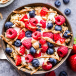 Berry Quinoa Breakfast Bowl with a small bowl full of almonds and a spoon with yogurt on it