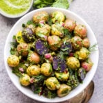 Chimichurri Potato Salad in a white bowl with spoons and extra chimichurri sauce in a small bowl on the side.