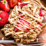 A slice of Strawberry Vanilla Baked Oatmeal on a wooden plate with strawberries on the side.