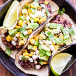 Two Black Bean Tacos with Avocado Corn Salsa overhead photo in cast iron skillet with lime wedges.