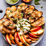 Grilled Peach and Burrata Crostini on round serving plate drizzled with pesto and balsamic glaze