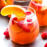 Peach Rosé Sangria in stemless glass garnished with a peach slice and fresh raspberries.