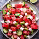 Watermelon Salad with Cucumber and Feta overhead photo of salad on grey plate with serving spoons and halved lime on the side