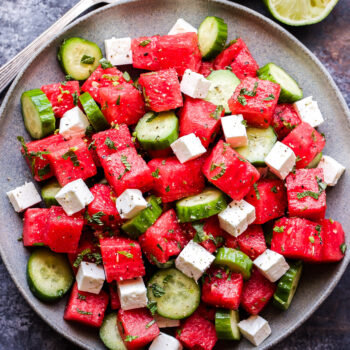 Watermelon Salad with Cucumber and Feta overhead photo of salad on grey plate with serving spoons and halved lime on the side
