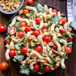 Overhead photo of Tomato, Arugula and Goat Cheese Pasta in bowl with a small bowl of walnuts on the side and cherry tomatoes.