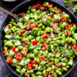 Asian Edamame Salad in black serving bowl with spoon in bowl and bowl of vinaigrette on the side.