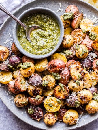 Parmesan Pesto Roasted tri-colored baby Potatoes on a gray plate with a bowl of pesto on the plate.