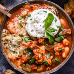 Slow Cooker Italian Turkey Chili in bowl with spoon topped with a dollop of ricotta and garnished with basil leaves.