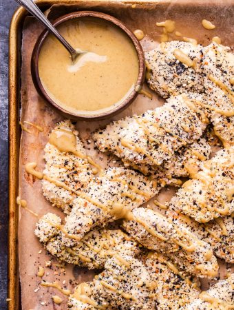 Everything Bagel Chicken Tenders on parchment lined sheet pan with a small bowl of maple mustard dipping sauce.