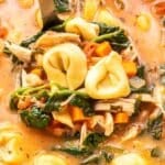 Ladle scooping up Tuscan Chicken Tortellini Soup out of a soup pot.