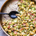 Brussels Sprouts and Bacon Pesto Pasta in metal skillet with black serving spoon. A portion of the pasta has been scooped out.