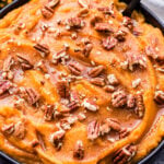 Cinnamon Maple Mashed Sweet Potatoes and Butternut Squash topped with chopped pecans in a black bowl with a black spoon in the bowl.