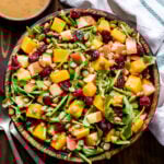 Butternut Squash Lentil Salad with cranberries, arugula, pepitas, apples in a wooden bowl. Serving spoons and a small bowl of cider vinaigrette next to the salad bowl.