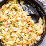 Vegan Cauliflower Gratin in cast iron skillet with some scooped out and a black spoon in the skillet.