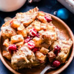 A piece of Cranberry Apple French Toast Casserole drizzled with vanilla glaze on a wood plate with a fork.
