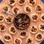 Cranberry Maple Pecan Baked Brie Bites on a round wooden serving platter with a bowl of the cranberry pecan topping in the middle.