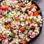 Greek Chickpea Salad with Tzatziki Dressing in black bowl with a small bowl of dressing behind it and serving spoons in the salad.