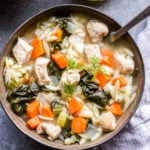 Lemon Chicken, Spinach and Orzo Soup in a bowl with a spoon and lemon half in the background.
