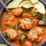 Mexican Meatball Soup in bowl with spoon topped with cilantro and avocado slices.