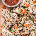 Sesame Crusted Chicken Tenders on parchment paper with a bowl of sweet chili sauce behind them.