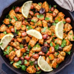 Lemon Herb Chicken and Potatoes with lemon wedges on top in a black skillet.