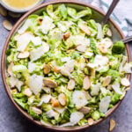 Lemon Parmesan Shaved Brussels Sprouts Salad in serving bowl with spoons and bowl of vinaigrette behind it.
