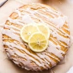Overhead photo of a round Lemon Yogurt Cake drizzled with white glaze and topped with three lemon slices.