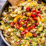 Creamy Chicken Enchilada Pasta in pan with a wooden serving spoon. Topped with tomatoes, olives, green onions and cilantro.