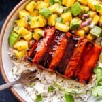 Overhead photo of Honey Sriracha Salmon with Pineapple Avocado Salsa in a white bowl on top of rice with a fork in the bowl.