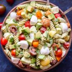 Overhead photo of Tomato Avocado Pasta Salad with mozzarella chunks and basil leaves in a white bowl with two spoon.