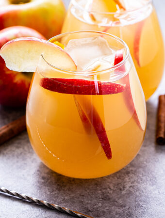 Front view of a glass filled with apple cider sangria. Apple slices are in the cocktail and the rim of the glass has an apple slice for garnish.