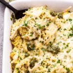Cheesy Pesto Chicken Spaghetti Squash in a white casserole dish with a black serving spoon in it and a bowl of pesto behind the dish.