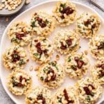 Sun Dried Tomato Pesto Goat Cheese Bites on a white plate with a spoon of pesto and a bowl of pine nuts behind the plate.