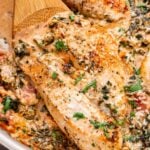 Wooden spoon hold one of the chicken breasts in the Creamy Italian Chicken Skillet.