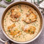 Creamy Mustard Chicken in metal skillet with a bowl of chopped parsley behiind it.