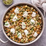 Skillet with Roasted Cauliflower and Chickpea Pesto Pasta in it and a small bowl of pesto with a spoon in it behind the skillet.