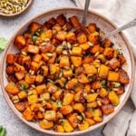 Sweet and Spicy Roasted Butternut Squash in a white bowl with spoons. A bowl of pepitas behind it.