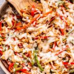 Chicken Cheesesteak Skillet with red and green peppers, onions and melted provolone cheese on top. A wooden spoon is in the skillet.