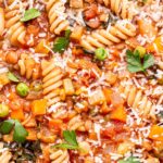Lentil Minestrone Soup with rotini pasta in a white bowl topped with parmesan cheese and parsley.